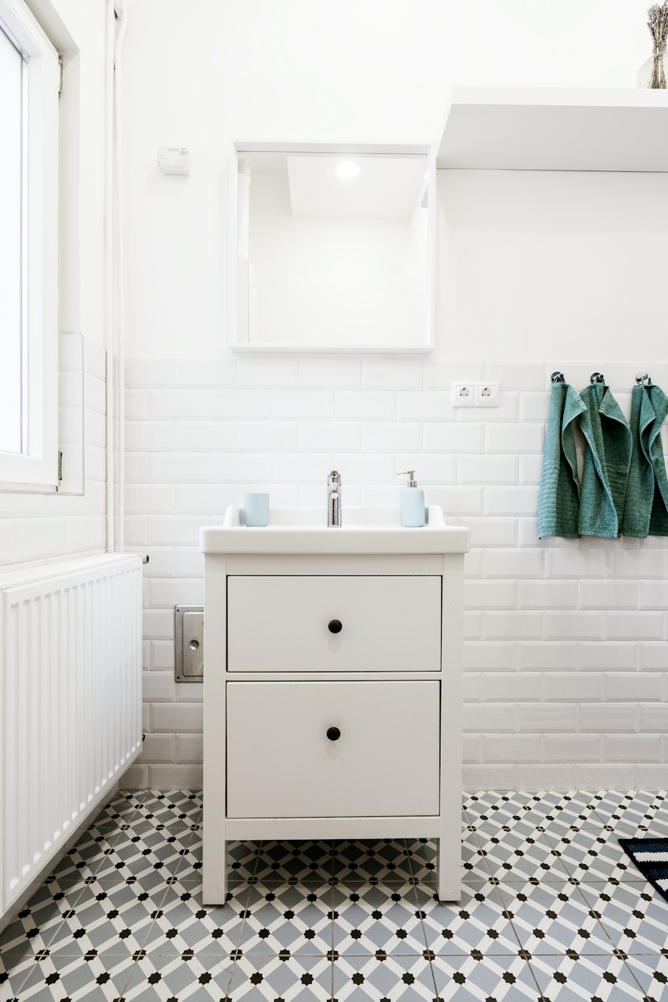Bagno moderno con mobiletto bianco e piastrelle geometriche sul pavimento.