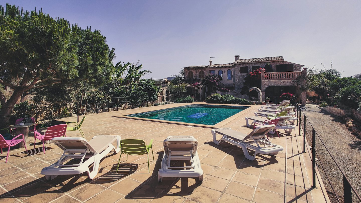 Area piscina di una villa in pietra con sedie a sdraio e cielo blu.