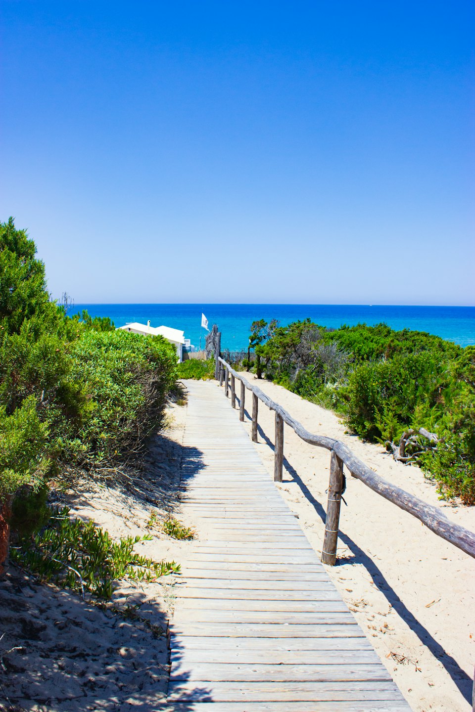 Passerella in legno tra dune sabbiose che conduce al mare turchese.